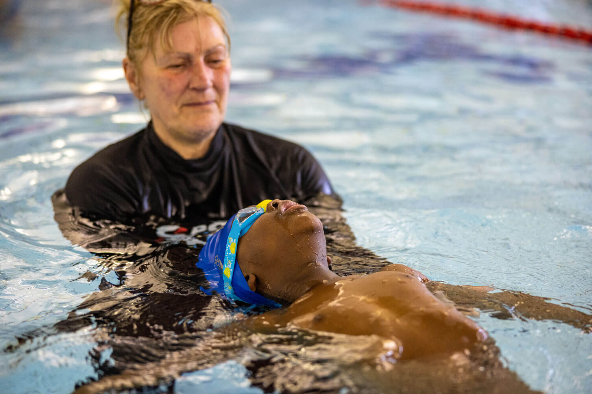 Teacher supports head of swimmer doing backstroke
